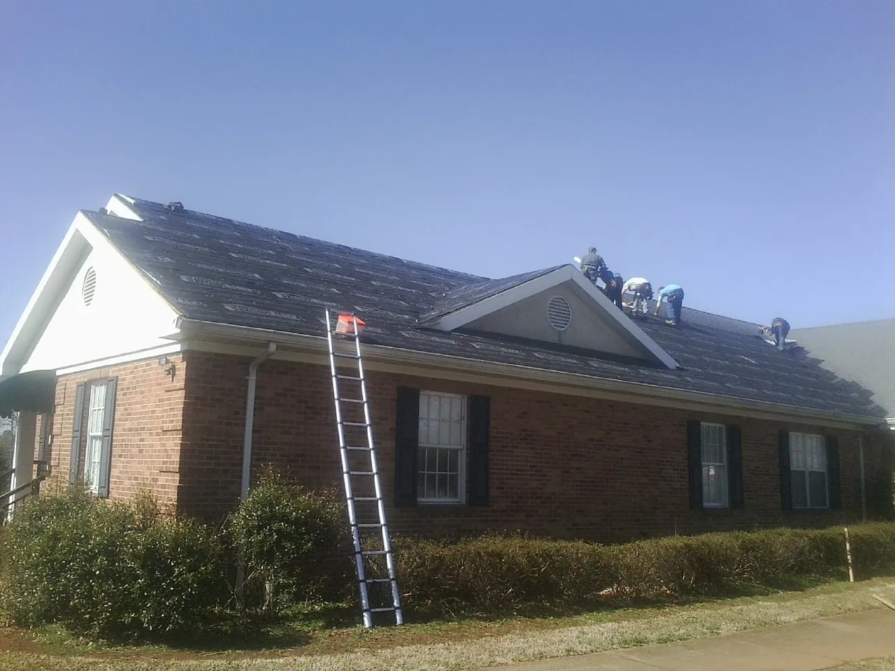Crew tearing shingles off a brick ranch roof with a ladder set — Emergency Roof Repair work by our crew in Louisville
