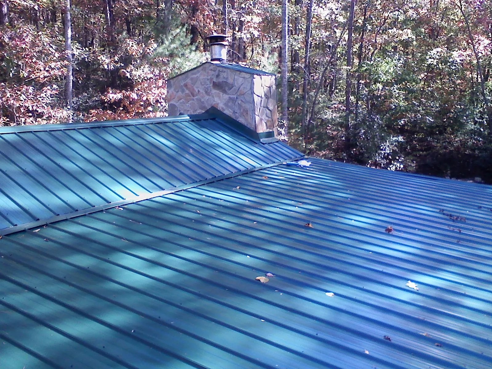 New green metal roof and stone chimney surrounded by autumn woods in Louisville