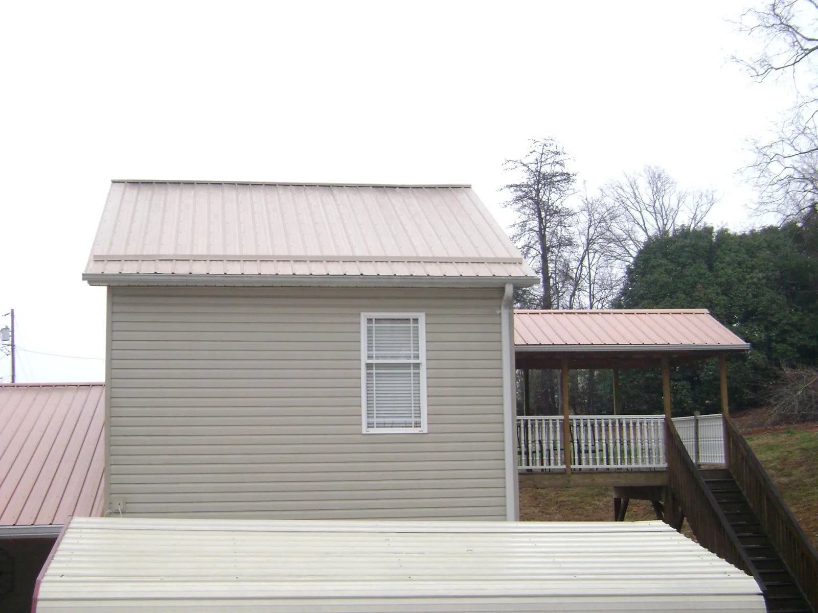 Tan metal roofs on a two story addition and attached porch, from a Roof Replacement job in Louisville